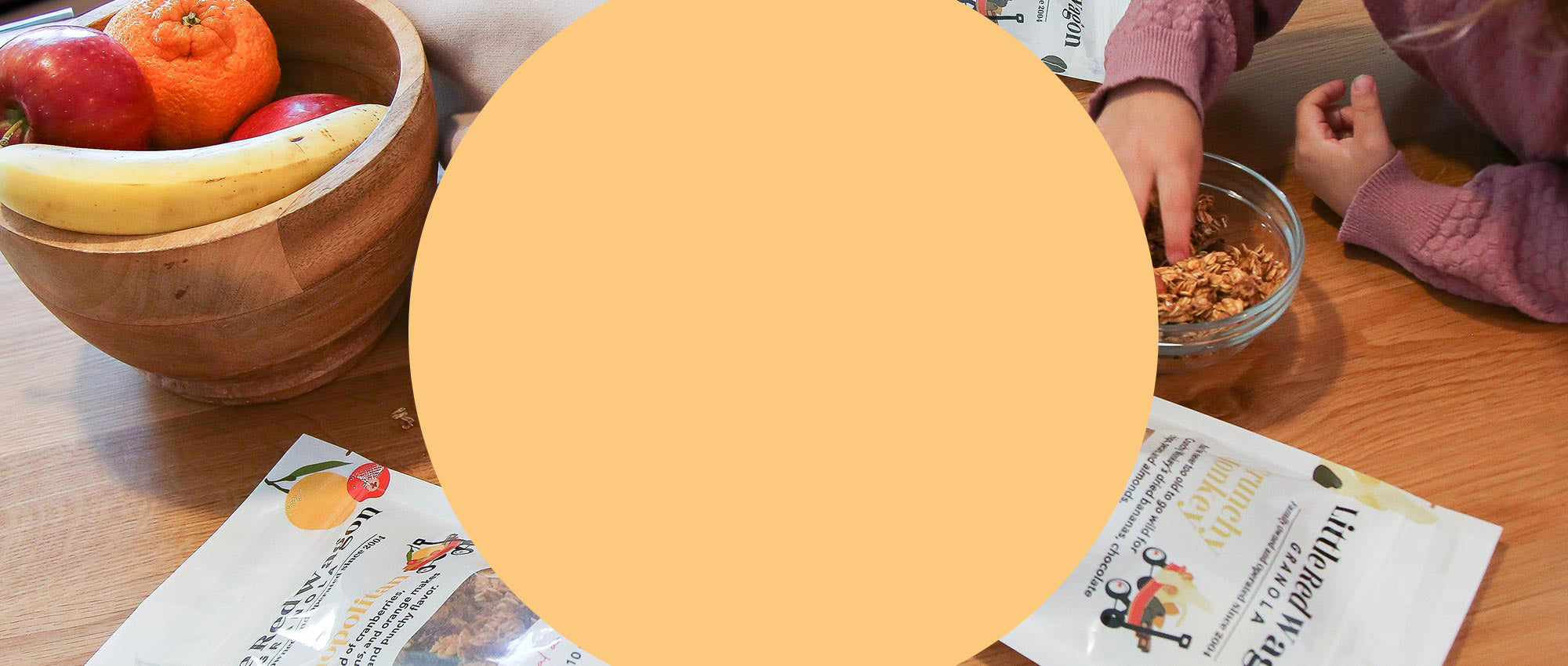 Person eating from a bowl with a wooden bowl of fruit and a table with papers in the background.