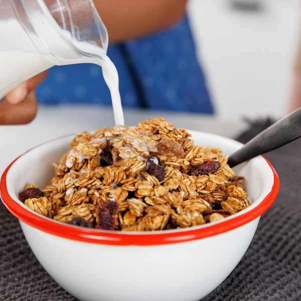 Bowl of granola with raisins being poured with milk