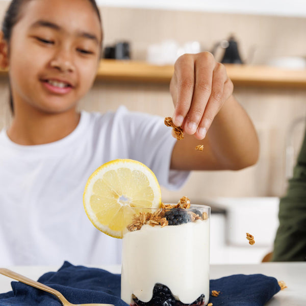 Person adding toppings to a glass of yogurt with a lemon slice and blueberries.