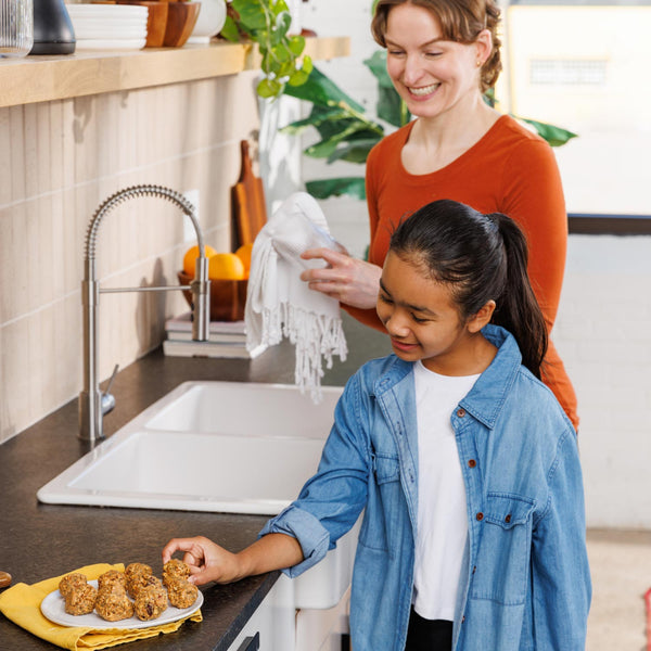 Woman and young girl in a kitchen preparing food together.
