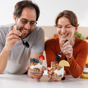 Man and woman enjoying yogurt parfaits with spoons, smiling.